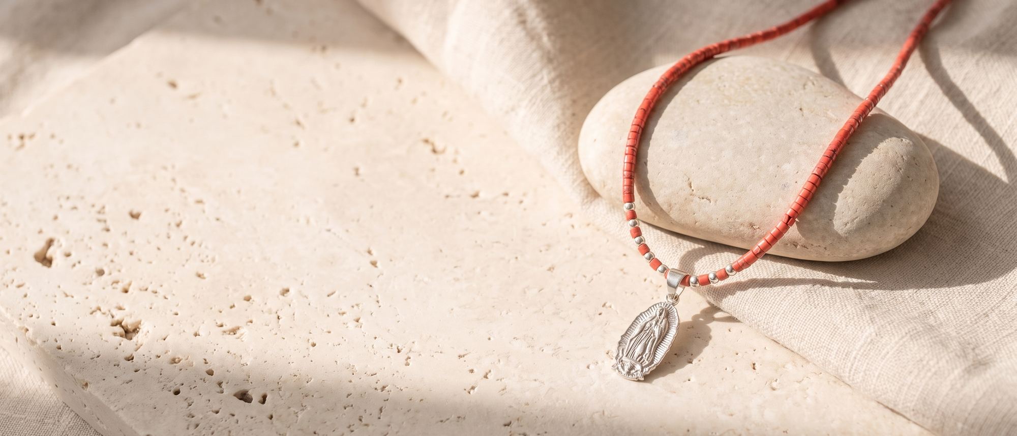 Collar de coral con medalla de la Virgen de Guadalupe sobre piedra y lino